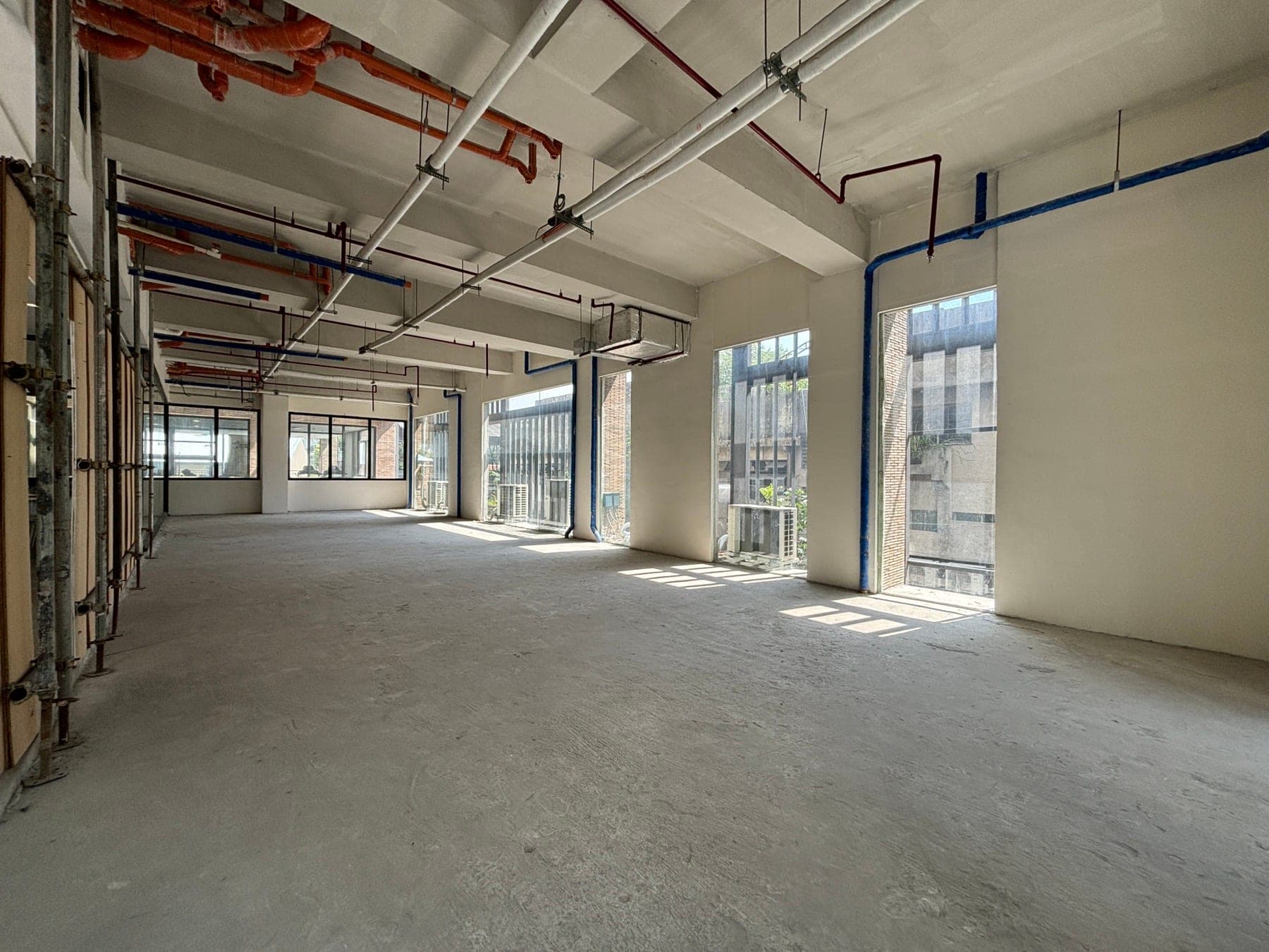 Wide view across the unfinished floor slab towards a run of full-height windows