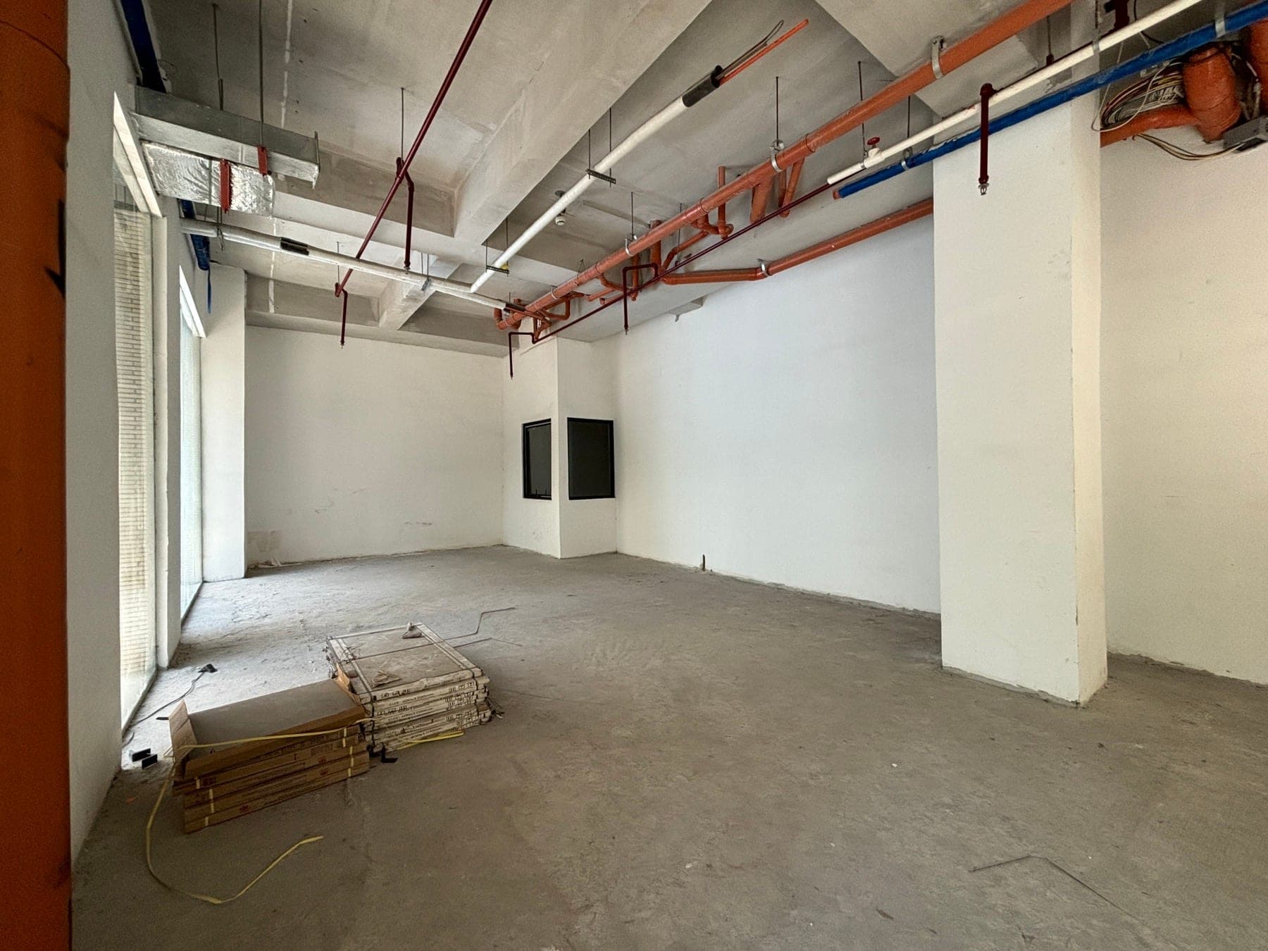 Blank end wall with a service opening, ductwork above and stacked fit-out materials on the floor